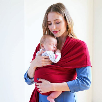 Bébé endormi contre sa maman en écharpe de portage rouge, moment d’allaitement paisible et sécurisé à la maison.