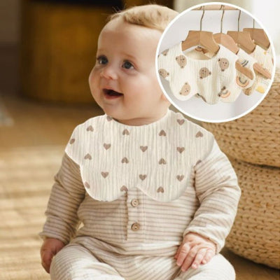Bébé blond souriant portant un bavoir bébé manche longue en coton avec motif cœurs marrons, bavoir tissu repas confortable.