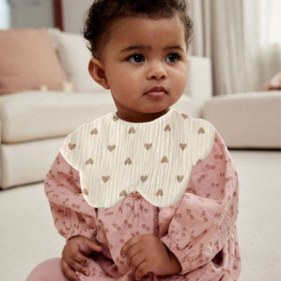 Bébé métisse portant un bavoir bébé manche longue en coton bio motif cœurs, bavoir coton bébé confortable et absorbant pour repas.
