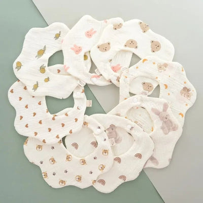 Lot de bavoirs bébé manche longue en coton, motifs variés (lapins, ours, fruits, cœurs, arc-en-ciel) disposés en cercle, bavoir tissu bébé couture.