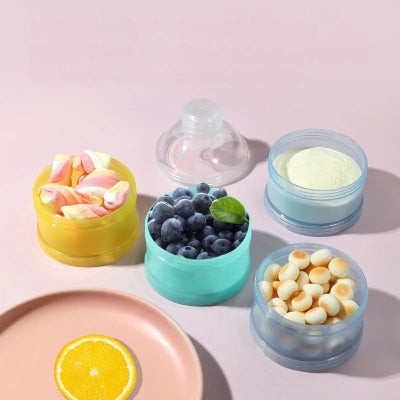 Quatre compartiments ouverts de la boite doseuse lait contenant différents aliments pour bébé : poudre, fruits, bonbons et biscuits.