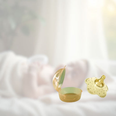 Bout de seins en silicone couleur ambre avec étui de transport, posé sur lit à côté d’un bébé, solution idéale pour un allaitement en déplacement.
