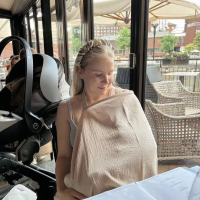 Maman allaitant son bébé en terrasse avec la cape d’allaitement beige Voilâme™, assurant discrétion et confort en public.