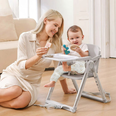 Chaise haute évolutive bébé pliable utilisée comme siège de table bas, avec plateau repas transformé en espace de jeux éducatifs. Maman joue avec son enfant assis confortablement dans une chaise haute bébé design et sécurisée.