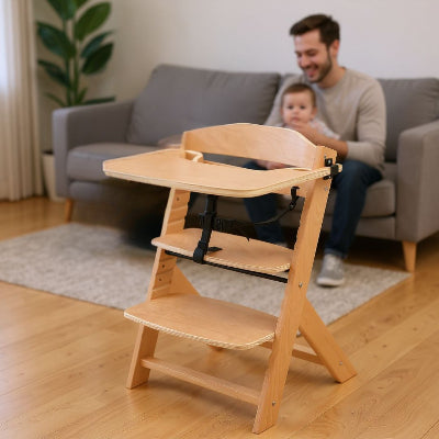 Papa avec son bébé dans le salon, chaise haute bébé bois en premier plan, évolutive et sécurisée pour repas et jeux.