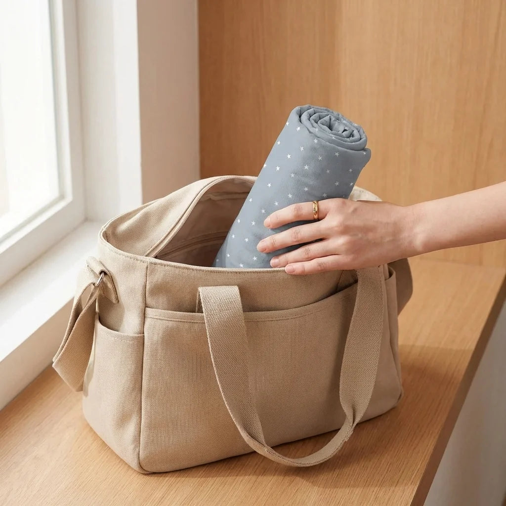 Châle allaitement DouxVoile™ Géo bleu gris roulé compact glissé dans sac à langer beige — format pratique pour toutes les sorties