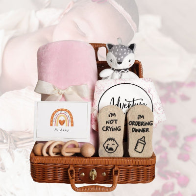 Coffret naissance bébé en version fille, devant une silhouette de bébé endormie, ambiance douce avec fond rose et pétales décoratifs.