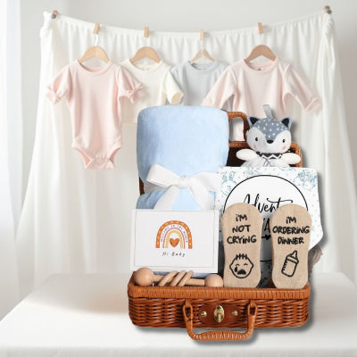 Coffret Naissance Bébé présenté sur une table avec en arrière-plan des bodies suspendus, parfait pour une baby shower ou un cadeau de maternité