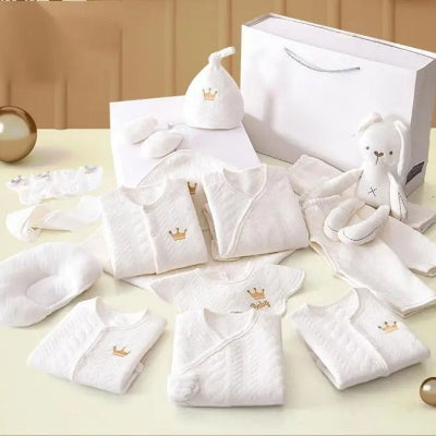 Contenu détaillé du coffret naissance bébé avec pyjamas, ensembles velcro, chaussettes, bonnet et jouet peluche, étalés sur une surface douce.