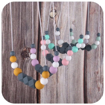 Ensemble de colliers d’allaitement multicolores suspendus sur un fond en bois naturel, mettant en avant la variété de styles disponibles
