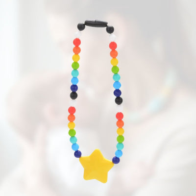 Collier d’allaitement arc-en-ciel avec étoile jaune en silicone alimentaire, porté durant un moment de câlin, pour éveiller la curiosité de bébé et soulager les poussées dentaires.