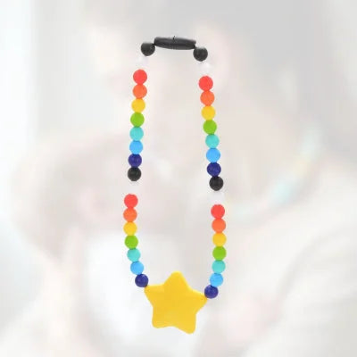 Collier d’allaitement arc-en-ciel avec étoile jaune en silicone alimentaire, porté durant un moment de câlin, pour éveiller la curiosité de bébé et soulager les poussées dentaires.