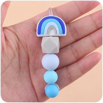 Collier dâallaitement en silicone bleu glacier tenu dans une main adulte, mettant en valeur les perles souples apaisantes pour les gencives de bĂ©bĂ© durant les poussĂ©es dentaires.