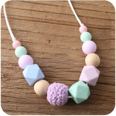 Collier d’allaitement en perles pastel lilas, vert menthe et rose tendre, stimulant la motricité fine de bébé et offrant un soulagement pendant les poussées dentaires.