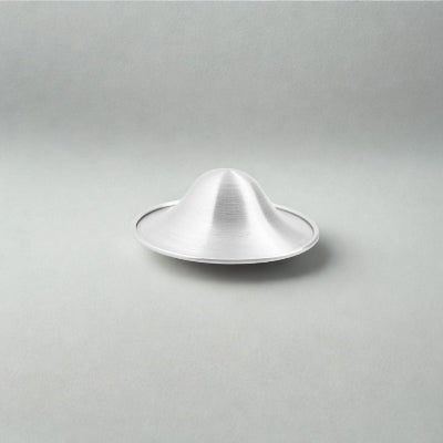 Présentation d’une coupelle d’allaitement en argent sur fond neutre mettant en valeur son design concave et respirant