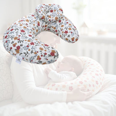 Maman souriante tenant bébé avec un coussin d’allaitement fleuri aux tons automnaux, pour une séance d’allaitement sereine et stable.