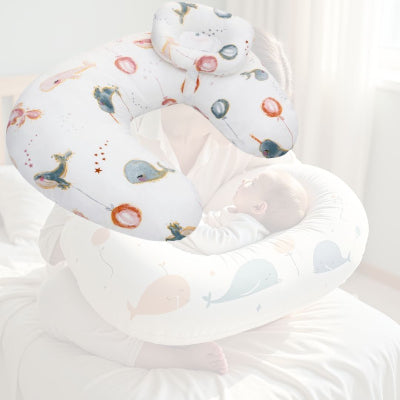 Maman allaitant son bébé avec un coussin d’allaitement motif ballons et baleines, garantissant un soutien optimal et une position ergonomique pendant la tétée.