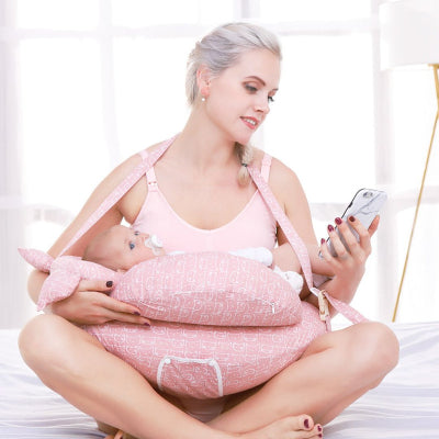 Maman utilisant un coussin d’allaitement rose avec sangle pour allaiter son bébé tout en gardant les mains libres, dans une ambiance détendue à la maison.
