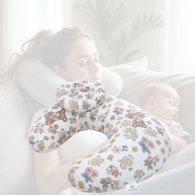 Jeune maman utilisant un coussin d’allaitement fleuri à motif ourson, pour soulager son dos et caler son bébé durant une sieste ou une tétée.