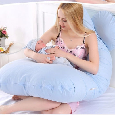 Jeune maman tenant son bébé dans les bras tout en étant soutenue par un coussin de grossesse bleu pastel, parfait pour l’allaitement et le cocooning.