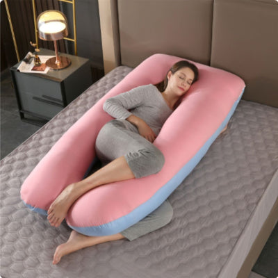 Femme enceinte dormant sur le côté avec un coussin de grossesse rose et bleu en forme de U, idéal pour soulager le dos et le ventre.