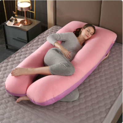 Femme enceinte en position fœtale utilisant un coussin de grossesse rose et violet pour améliorer la circulation et réduire la pression du bassin.
