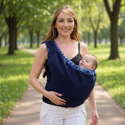 Femme souriante avec bébé en écharpe de portage allaitement bleu marine, promenade dans un parc, portage physiologique et allaitement discret.