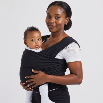 Maman souriante tenant bébé en écharpe de portage noire, posture droite favorisant le contact peau à peau et l’éveil du bébé.