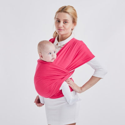Maman debout portant bébé en écharpe de portage rose, position ventrale latérale pour allaitement pratique et mains libres.
