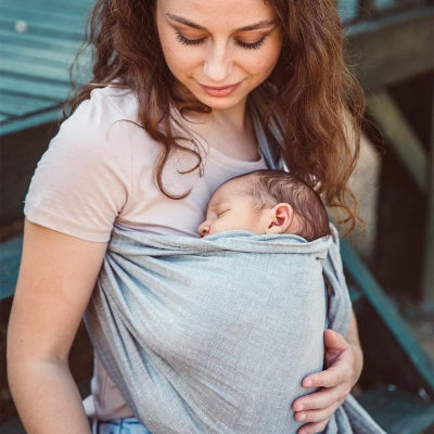 Jeune maman tenant son bébé dans une écharpe de portage sans nœud, position physiologique idéale pour le confort et l’allaitement.