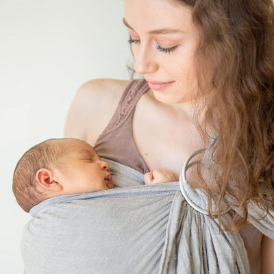Maman portant son nouveau-né avec une écharpe de portage sans nœud grise équipée d’anneaux métalliques pour un ajustement rapide.