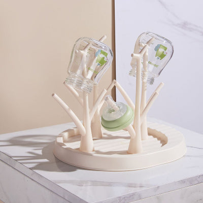 Égouttoir biberon DryBébé™ couleur crème posé sur un plan marbré, avec deux biberons en verre et une tétine, pour une organisation élégante.