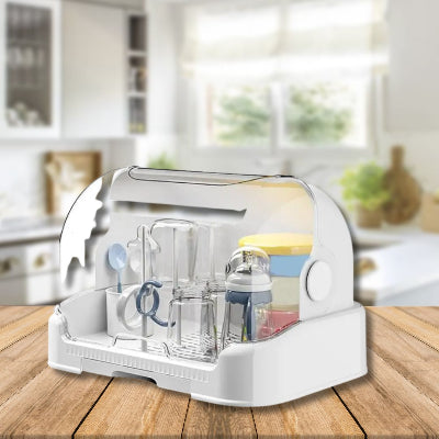 Égouttoir biberon posé sur un plan de travail en bois, équipé d’un couvercle protecteur et de compartiments modulables pour sécher jusqu’à 8 biberons et accessoires.