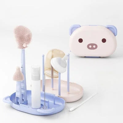 Goupillon biberon complet en bleu pastel avec flacon savon, mini-brosses et égouttoir, dans une boßte rigolote rose cochon pour jeunes parents.