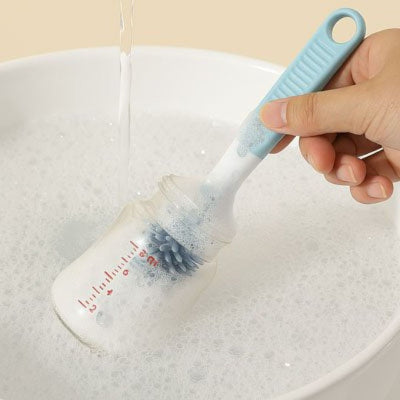 Goupillon pour biberon en silicone bleu utilisé pour nettoyer l’intérieur d’un biberon rempli de mousse savonneuse.