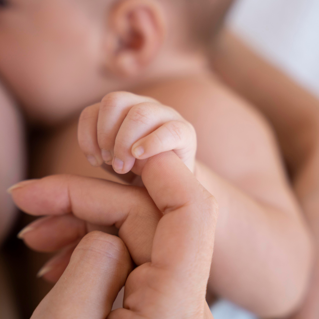 Main de bébé serrant le doigt de sa maman pendant l’allaitement, symbole du lien affectif.