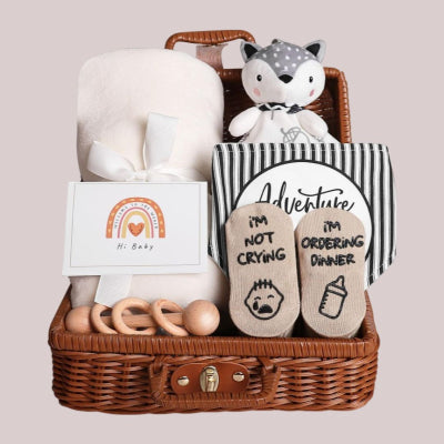 Coffret naissance bébé Toudou™ posé sur fond neutre, avec couverture blanche en tissu doux, peluche renard, chaussettes rigolotes, jouets en bois naturel et carte de vœux, idéal comme idée cadeau bébé.