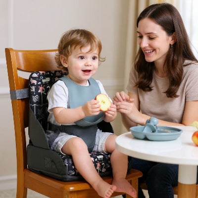 Chaise rehausseur bébé pliable motif animaux pastel, bébé mange une pomme à table avec sa maman, siège repas bébé confortable et sécurisé.