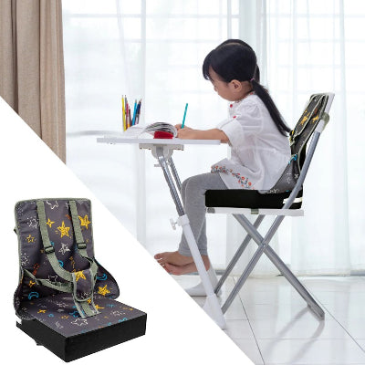 Fille assise sur un coussin réhausseur chaise enfant, utilisant le rehausseur de chaise bébé comme coussin surelevateur pour écrire à la table.