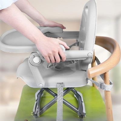 Installation d’un réhausseur de chaise bébé gris avec ceintures de sécurité réglables fixées sur une chaise adulte, siège de table bébé stable et pratique pour les repas.