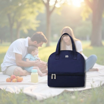 Sac isotherme bébé bleu posé sur une couverture de pique-nique avec un bébé et ses parents, idéal pour les repas en plein air.
