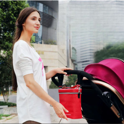 Sac isotherme Bebe rouge suspendu à une poussette grâce à sa bandoulière multifonction, pratique pour les trajets du quotidien avec bébé.
