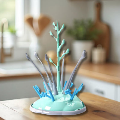 Sèche biberon design en forme d’arbre vert menthe et gris, posé sur un plan de travail en bois dans une cuisine lumineuse, idéal pour sécher biberons et tétines tout en gardant l’espace propre et organisé.
