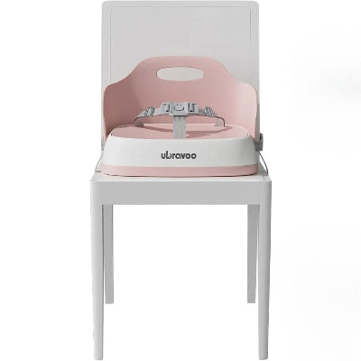Siège repas bébé rose fixé solidement sur une chaise blanche, réhausseur chaise enfant pliable avec harnais de sécurité et dossier ergonomique pour repas confortables à table.