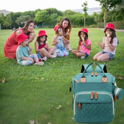 Sac à dos à langer BabyNest™ posé dans un parc lors d’un moment convivial avec des enfants et des parents partageant un goûter.

