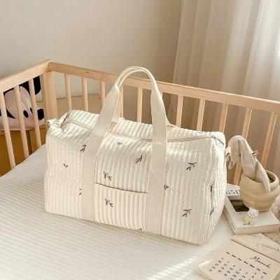 Un sac à langer DreamNest™ Olive Elegance délicatement posé dans une chambre de bébé, offrant une touche de sérénité et d'élégance naturelle grâce à son motif d'olives brodées.