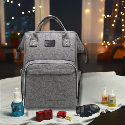 Sac à langer SerenityPack™ en gris chic avec des accessoires de soin pour bébé, mis en scène dans une ambiance cosy et chaleureuse.