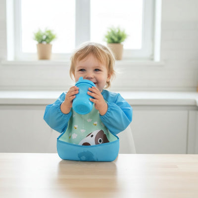 Bébé blond portant un bavoir à manche longue bleu motif chien, parfait pour les repas ou activités créatives, inclus dans un lot de bavoir bébé lavable et durable.