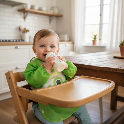 Bébé buvant au biberon tout en portant un bavoir à manche longue vert motif grenouille, un bavoir bébé naissance pratique et imperméable pour les repas.