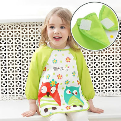 Fille portant un bavoir à manche longue hibou vert, avec un zoom sur la fermeture velcro, soulignant la praticité du bavoir manche longue bébé.